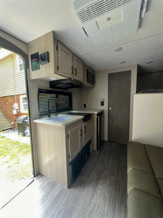 Modern RV rental interior with kitchen (sink, stove, microwave, fridge), AC, wood-look floor, sofa, and outdoor view.. Forest River Aurora Aurora 2025