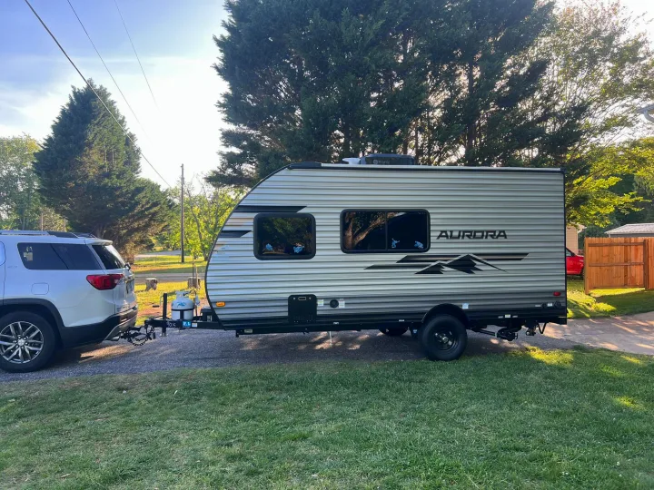 An Aurora travel trailer, an RV rental, is hitched to a white SUV on a sunny day, ready for camping adventures.. Forest River Aurora Aurora 2025