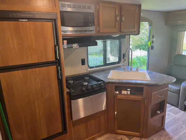 Well-equipped RV rental kitchen featuring a Dometic fridge, High Pointe microwave, stove, and sink area.. Keystone RV Springdale 2019