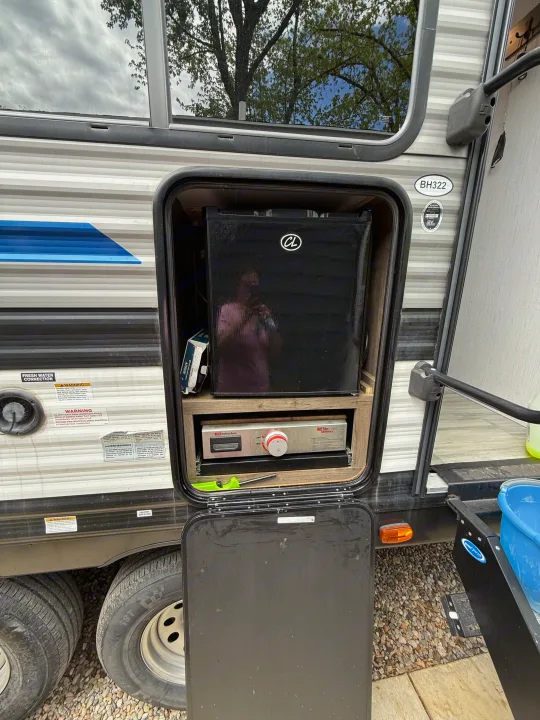 An RV rental with an open side compartment, revealing an outdoor kitchen featuring a black mini-fridge and built-in griddle.. 5SFPB372XME475890 Pioneer 2021
