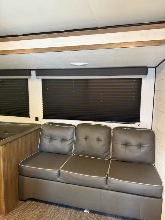 This RV rental interior showcases a cozy gray sofa with white piping, dark pleated window blinds, and light walls.. 5SFPB372XME475890 Pioneer 2021