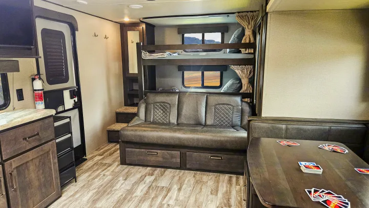 Cozy RV rental interior: bunk beds, sofa, dinette with UNO cards, and kitchen area. Ready for fun!. Grand Design Transcend Xplor 2022