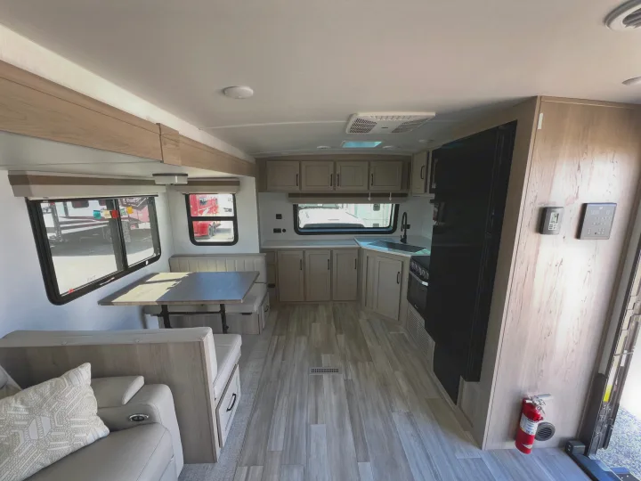 Inside a bright RV rental: open floor plan with kitchen, dining booth, and living area. Light wood cabinets and floor.. Forest River Rockwood Ultra Lite 2024