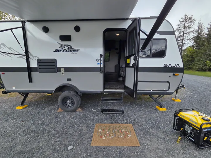 Experience your **rv rental** adventure! This Jay Flight Baja is set up at a gravel campsite with its awning extended, generator & mat.. Jayco Jay Flight SLX Baja Edition 2022