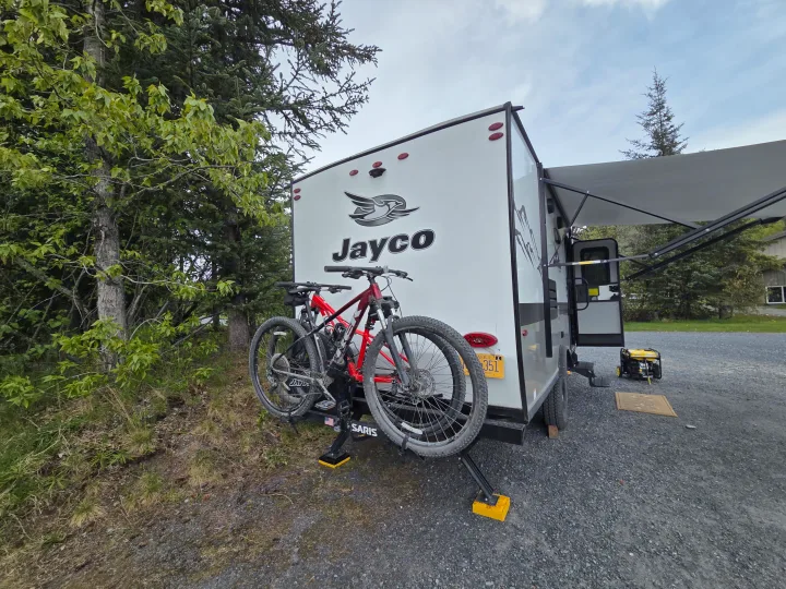 Alaska RV rental: Jayco travel trailer with bikes, awning, and generator parked on gravel at a campsite.. Jayco Jay Flight SLX Baja Edition 2022