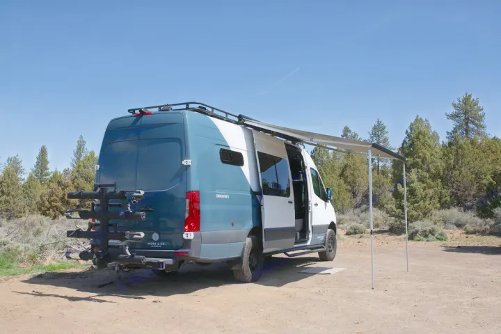 Custom blue & white RV rental van with extended awning & rear bike rack, parked on dirt in a natural setting.. Mercedes-Benz Sprinter 2020