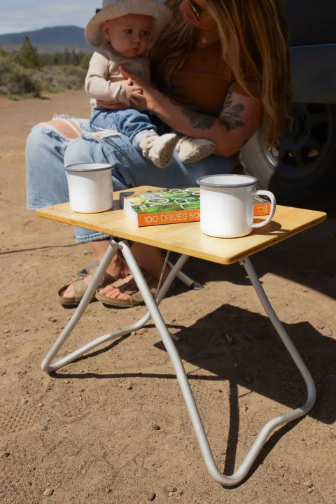 RV rental family enjoying outdoor relaxation with coffee & a book at a portable table amidst nature.. Mercedes-Benz Sprinter 2020