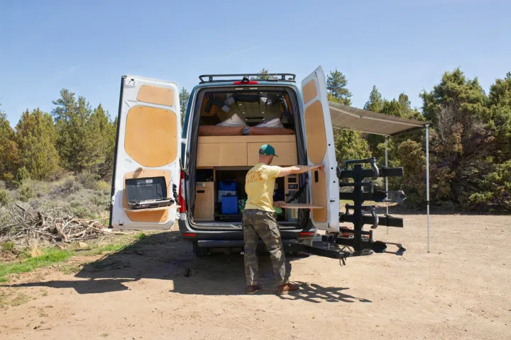 This RV rental camper van offers ultimate outdoor living! A man preps the integrated kitchen at the rear of the van.. Mercedes-Benz Sprinter 2020