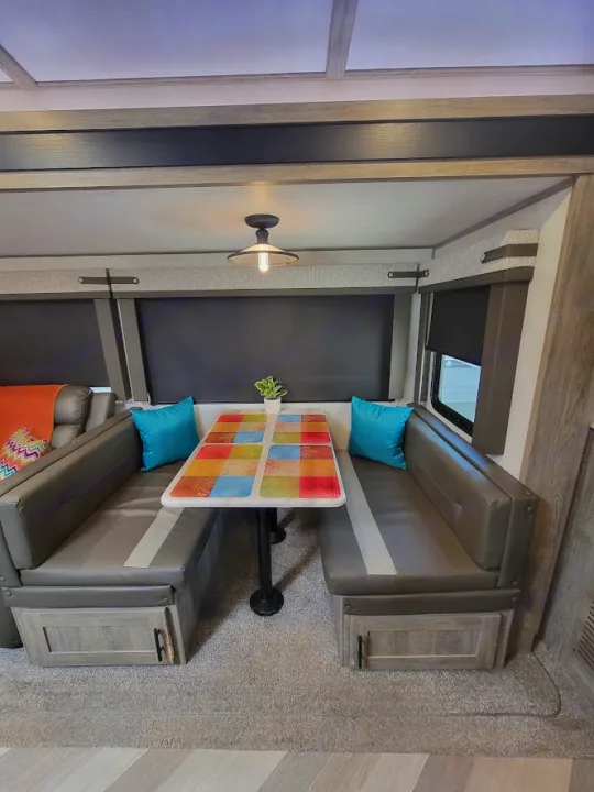 Modern rv rental interior: gray dinette booths, a vibrant table, and bright teal pillows for comfortable travel.. Forest River Salem Hemisphere 2021
