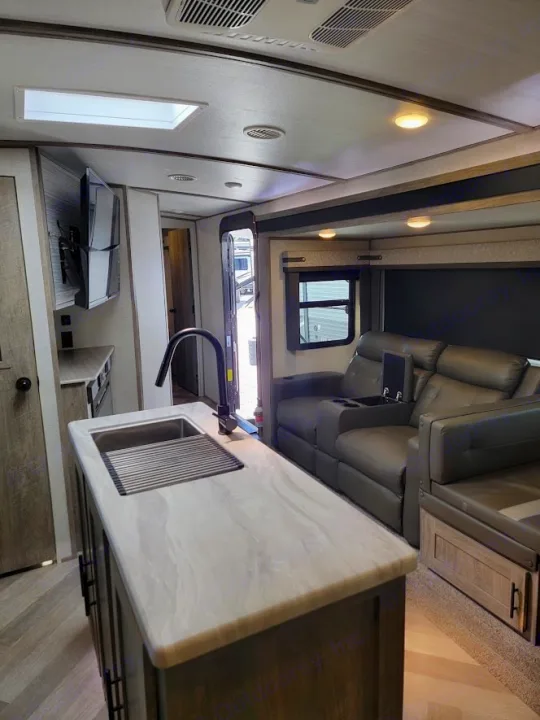 Modern RV rental interior showing a kitchen island with sink, TV, and comfortable living area with recliners and a dinette.. Forest River Salem Hemisphere 2021