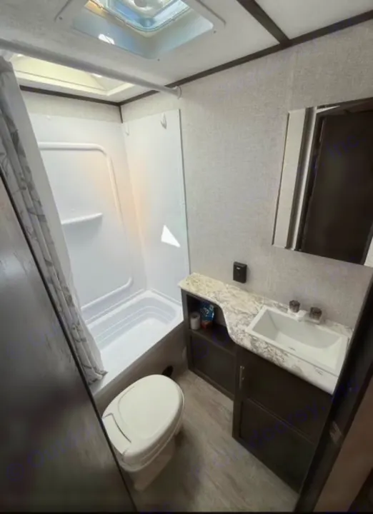 Inside an RV rental, this clean, compact bathroom features a shower/tub, toilet, and sink vanity.. Dutchmen 2340BHS 2020
