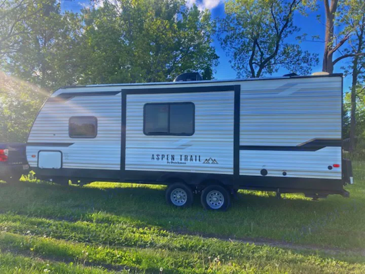 White Aspen Trail travel trailer RV rental parked on grass, connected to a truck. Perfect for your next adventure.. Dutchmen 2340BHS 2020