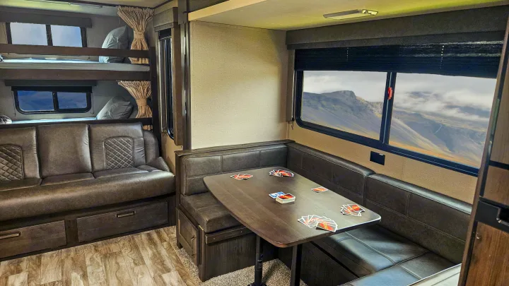RV rental interior: Bunk beds, sofa, & dining booth with UNO cards. Mountain views from windows, ideal for family travel.. Grand Design Transcend Xplor 2022