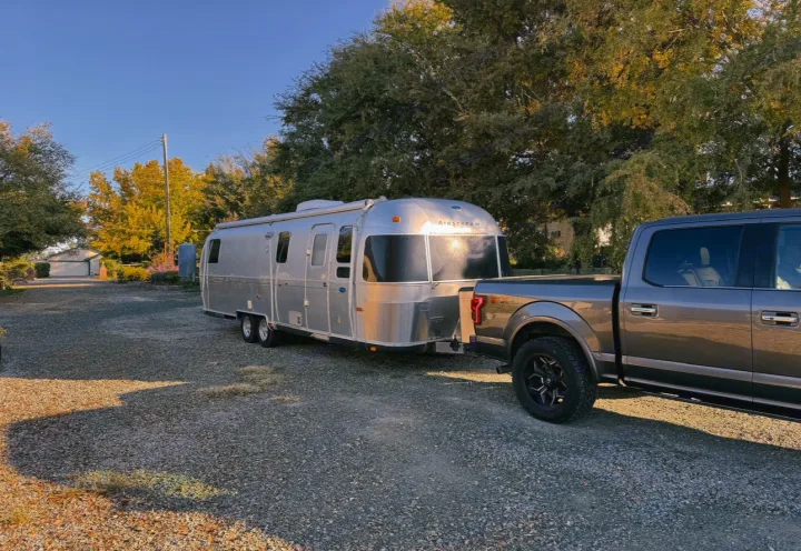 A gleaming silver Airstream RV rental hitched to a gray pickup truck on a sunny gravel lot, ready for travel.. Airstream Classic 2002