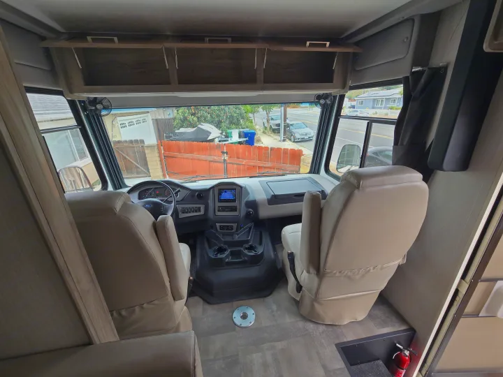 Spacious RV rental cockpit with tan seats, dashboard, and overhead storage, looking out the front window.. Coachmen Mirada 2020