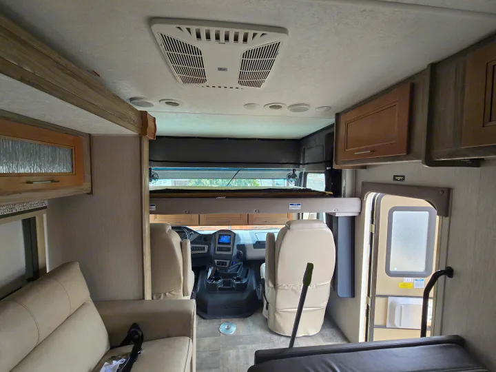 Spacious RV rental interior showing the cockpit, an overhead bunk bed, sofa, and ceiling-mounted AC unit.. Coachmen Mirada 2020
