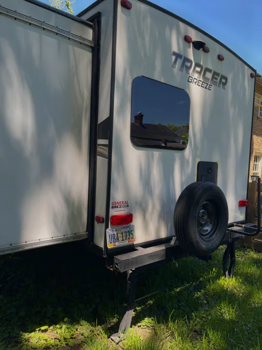 White Tracer Breeze RV rental, with a slide-out and spare tire, parked on grass. Ohio license plate visible.. Forest River Tracer Breeze 2019