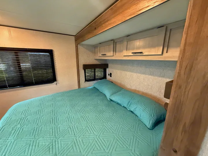 Comfortable RV rental bedroom featuring light blue bedding, dual windows, and ample storage, ideal for travel accommodations.. Heartland Zinger 320FB 2025