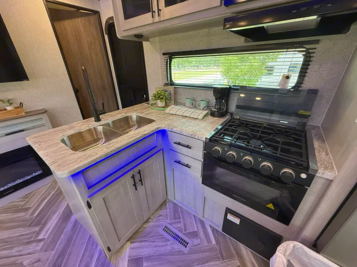 Compact RV rental kitchen with a modern design, double sink, gas range, and blue under-cabinet lights.. Heartland Zinger 320FB 2025
