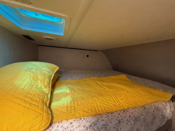 Compact RV rental sleeping area features a cozy bed with yellow bedding under a skylight.. Heartland Zinger 320FB 2025