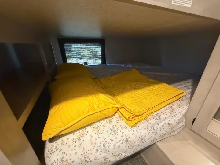 Cozy RV rental bunk bed featuring bright yellow blankets, floral sheets, and a window with blinds.. Heartland Zinger 320FB 2025