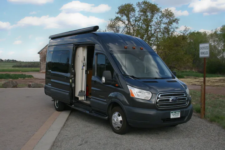Dark grey Ford Transit van, an RV rental, with open side door showing its interior, parked by an 'Oversized Vehicles' sign.. Forest River Coachmen Crossfit 2018