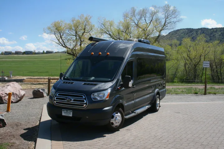 Dark grey Ford Transit van RV rental parked on pavers, with green fields and trees in the background.. Forest River Coachmen Crossfit 2018