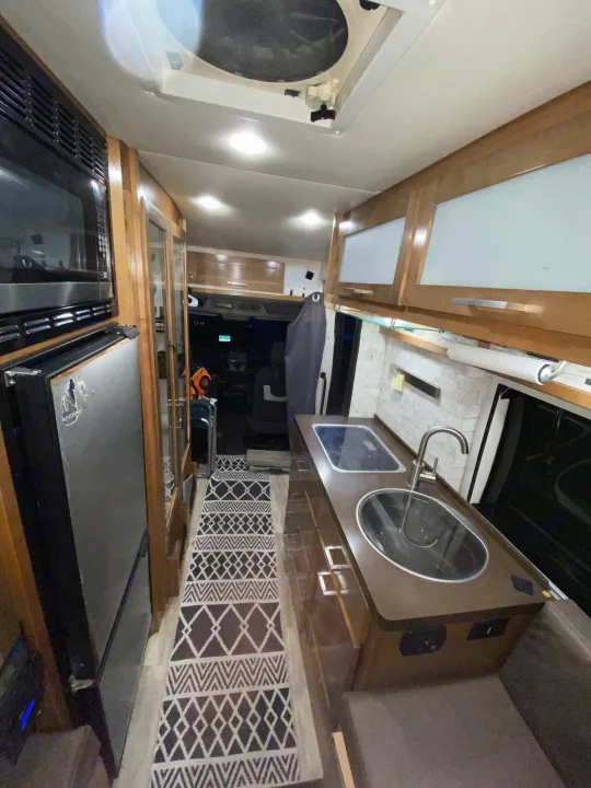 Inside an RV rental: Compact kitchen with sink & stovetop, microwave, fridge, and patterned runner.. Forest River Coachmen Crossfit 2018