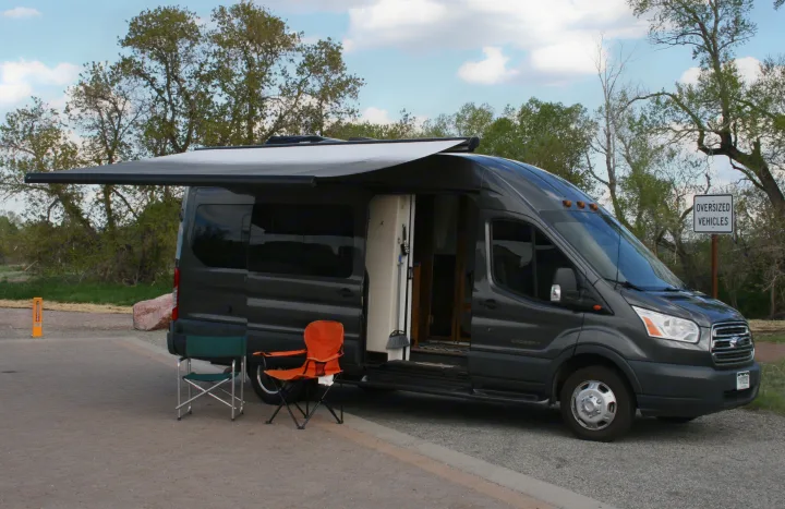 A modern grey Ford Transit camper van with an extended awning and open door, ideal for an RV rental adventure.. Forest River Coachmen Crossfit 2018