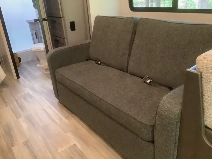 RV rental interior: Gray sofa with seatbelts, light wood floor, and bathroom in view. Ideal for road trips.. Forest River Solera 27 DSE 2023