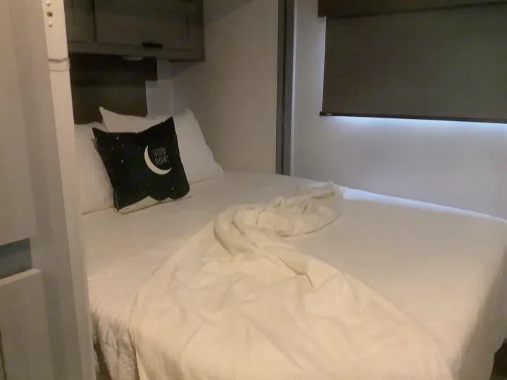 Clean RV rental bedroom with white bed, cozy "Good Night" pillow, and overhead storage. Ideal for travel.. Forest River Solera 27 DSE 2023
