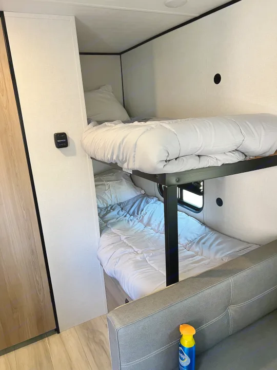 RV rental interior: cozy bunk beds with light bedding & a sofa, providing comfortable accommodations for travelers.. Coleman Lantern 17B 2025