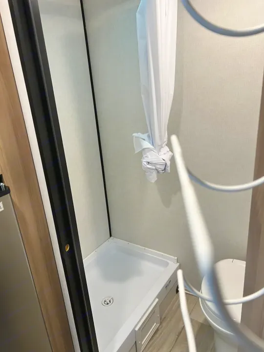 RV rental interior: A compact bathroom featuring a shower stall with a tied curtain and toilet.. Coleman Lantern 17B 2025