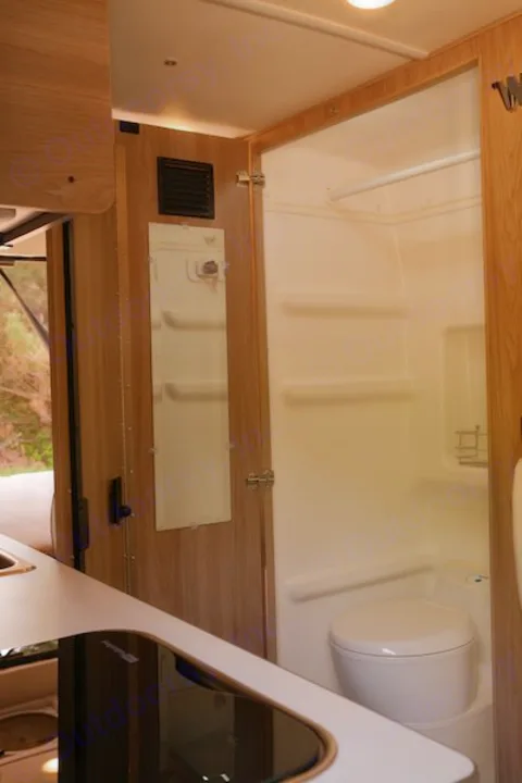 Compact RV rental interior featuring a kitchen with stovetop, sink, and an efficient wet bath with toilet and shower.. Winnebago Solis 2022