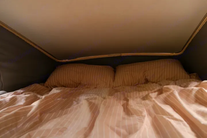 Cozy RV rental bed with striped bedding inside a pop-top camper. Ideal for comfortable rest on your travels.. Winnebago Solis 2022