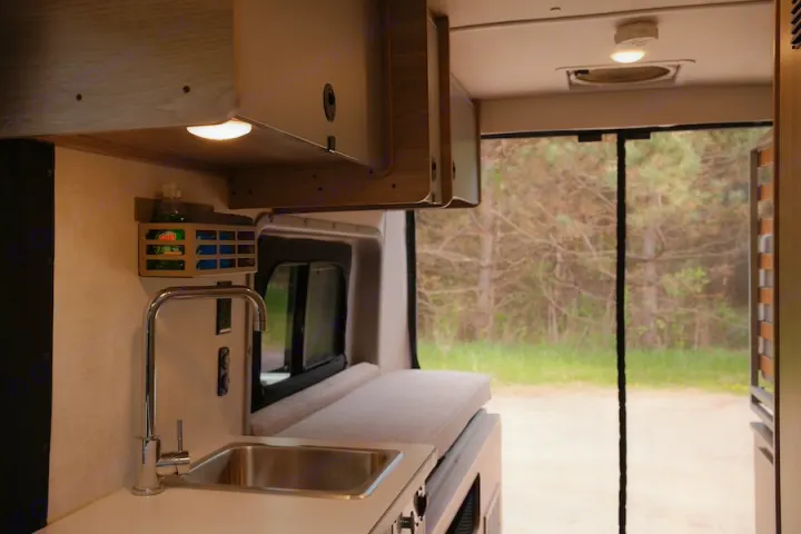 Inside a modern **rv rental**: compact kitchen with sink, bench, and rear mesh screen opening to nature. Ideal for adventures.. Winnebago Solis 2022