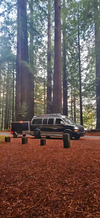 RV rental conversion van with trailer parked among towering redwood trees, ideal for forest camping.. Gmc Custom Savana 2007