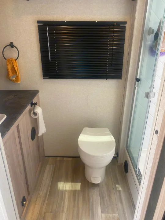 Inside an RV rental bathroom, featuring a white toilet, wood vanity, and glass shower enclosure. Functional and neat.. Coachmen Northern  Spirit Ultra Lite 2024