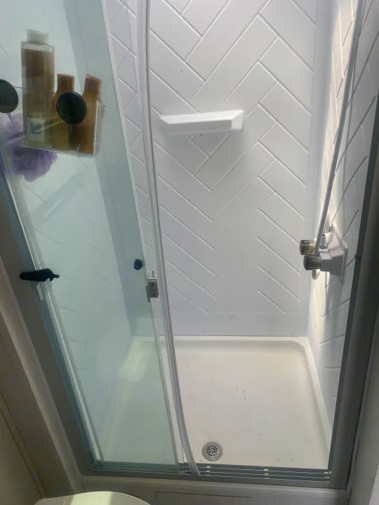 White herringbone shower in an RV rental, featuring a glass door, built-in shelf, and caddy with toiletries.. Coachmen Northern  Spirit Ultra Lite 2024