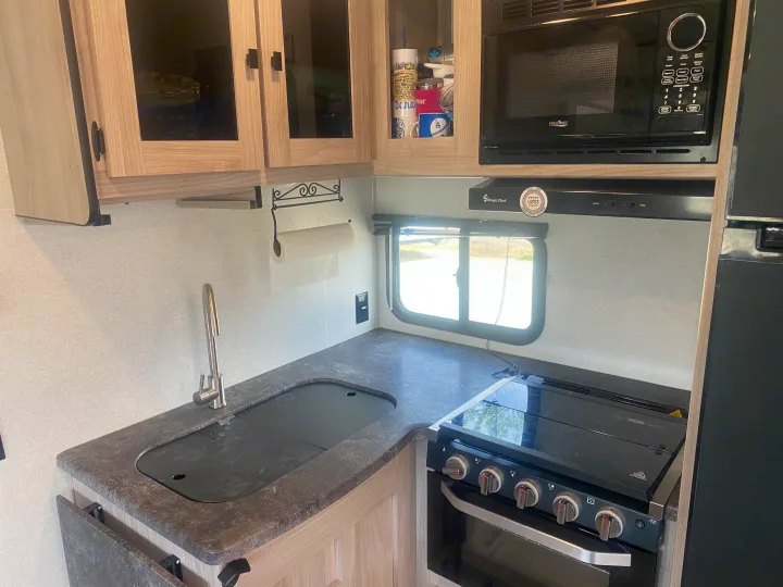 Inside a modern RV rental kitchen featuring a sink, microwave, stove, and light wood cabinets, ready for your next adventure.. Coachmen Northern  Spirit Ultra Lite 2024