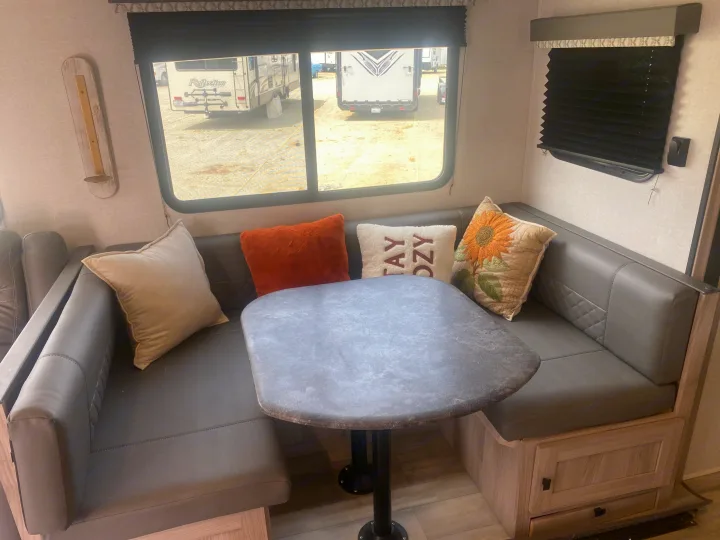 Cozy RV rental dinette with U-shaped seating, table, and decorative pillows, offering a view of other RVs outside.. Coachmen Northern  Spirit Ultra Lite 2024