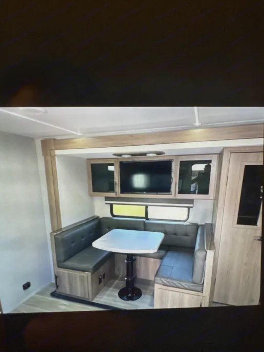 RV rental: Dinette in a recreational vehicle, featuring U-shaped seating, a white table, TV, and overhead cabinets.. Grand Designs 25DBE 2025