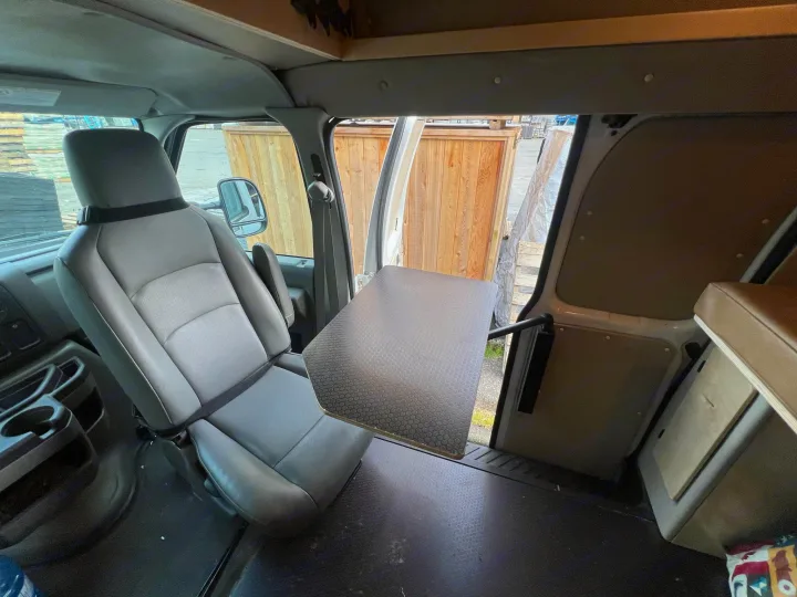 RV rental interior: swiveled passenger seat faces a side-mounted table, enhancing space for work or dining.. Ford E250 Eagle Camper 2012