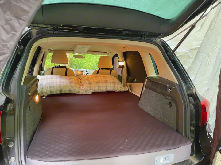 Compact RV rental option: Rear of an SUV converted for car camping, featuring a comfortable mattress, pillows, and attached tent.. Volkswagen Tiguan 2012