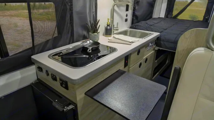 RV rental interior features a compact kitchen with an induction cooktop, sink, and cozy bed.. Winnebago Solis 2021