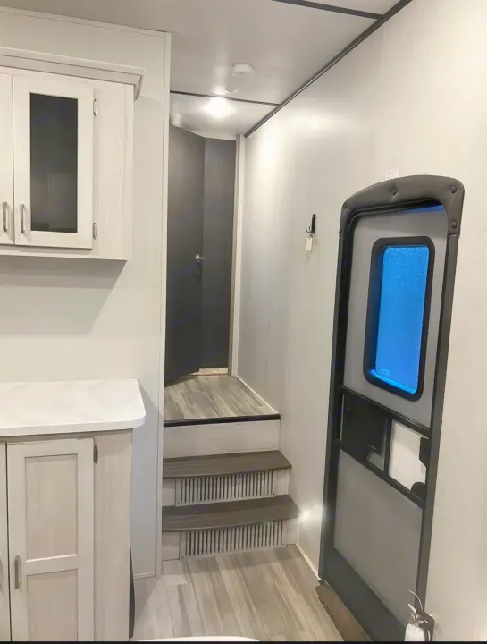 Inside an RV rental: light kitchen cabinets, stairs to a raised bedroom area, and the entry door with blue window.. Keystone RV Sprinter Campfire Edition 2021