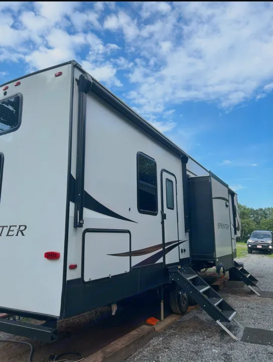 A white Sprinter travel trailer RV rental, with a slide-out, parked outdoors under a blue sky.. Keystone RV Sprinter Campfire Edition 2021