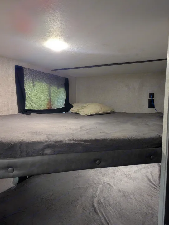 Cozy RV rental bunk beds with a window shade, pillow, and charging outlet. Provides comfortable sleeping space.. Keystone RV Bullet Crossfire 2020