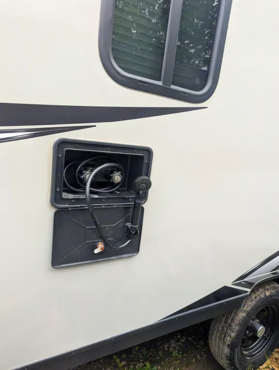 Outdoor shower on an RV rental. Visible open compartment with hose, showerhead, and water knobs on the light-colored exterior.. Keystone RV Bullet Crossfire 2020
