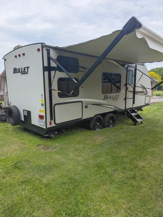 A light-colored Bullet Crossfire travel trailer, set up on grass with an extended awning, ready for your RV rental getaway.. Keystone RV Bullet Crossfire 2020